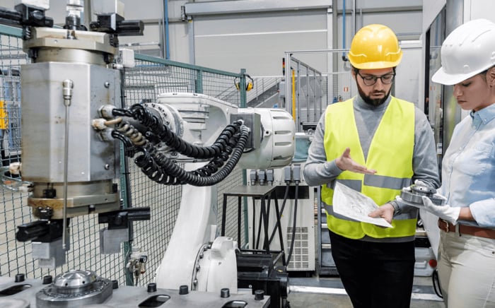 Zwei Ingenieure besprechen Details zur Fertigung eines Bauteils an einer industriellen Maschine in der Produktionshalle.