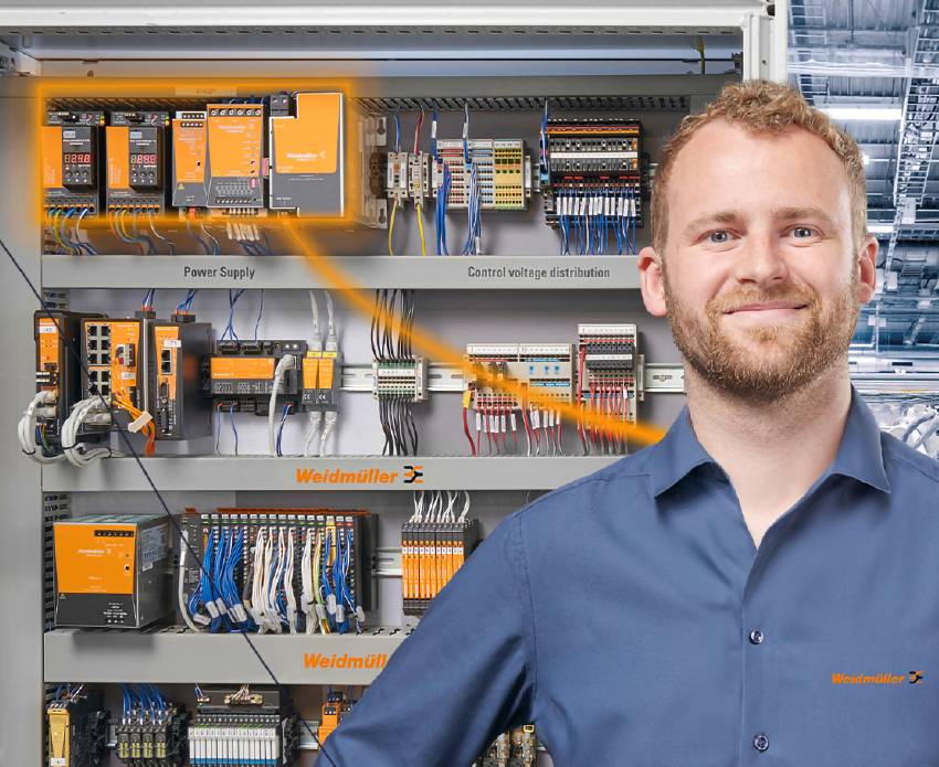 Ein lächelnder Mann in einem blauen Hemd steht vor einem Weidmüller-Schaltschrank mit orange hervorgehobener Stromversorgung.