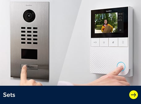  Zwei Hände interagieren mit DoorBird-Produkten: eine drückt den Klingelknopf einer silbernen Außenstation, während die andere einen blau leuchtenden Knopf auf einer weißen Innenstation mit Bildschirm betätigt, der einen Paketboten anzeigt.