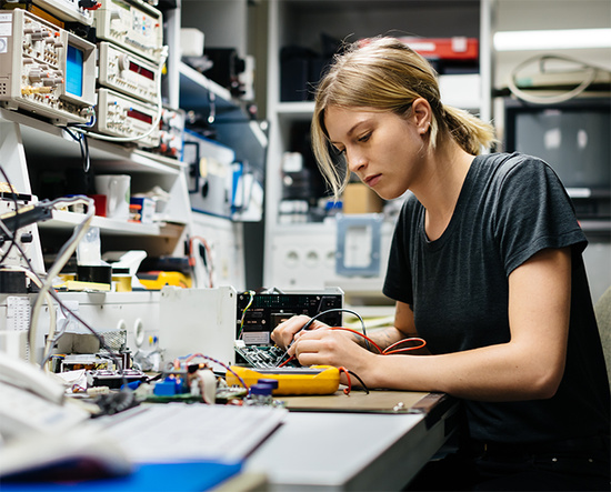 Junge Frau bei der Reparatur einer Elektronikplatine mit Messgeräten in einem Labor.