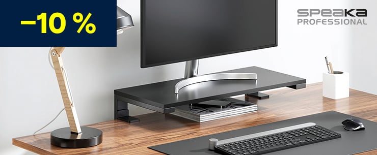 Schreibtisch mit Holzoberfläche, darauf ein Monitor auf schwarzer Monitorerhöhung, Tastatur, Maus, Schreibtischlampe und Stiftehalter, oben links ein „–10 %“-Hinweis und rechts das Logo „Speaka Professional“