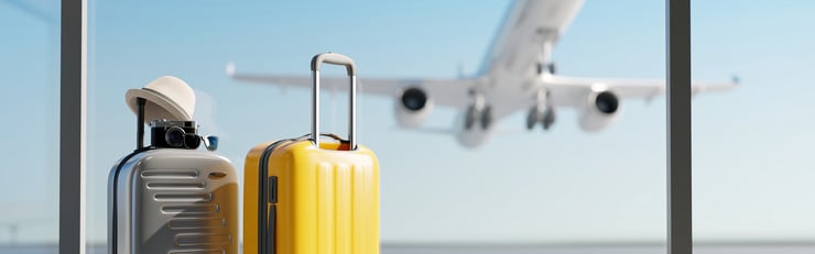 Zwei Reisekoffer stehen am Flughafenfenster, während ein Flugzeug im Hintergrund abhebt.