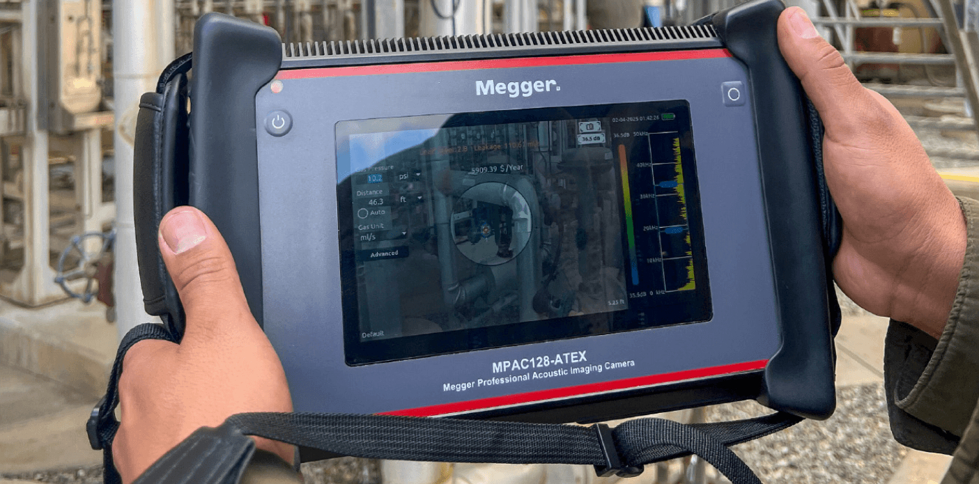 Eine Person hält eine professionelle Megger Akustikkamera (MPAC128-ATEX) in den Händen, deren Display eine Rohrleitung mit einer visualisierten Leckage und Frequenzdiagrammen zeigt.