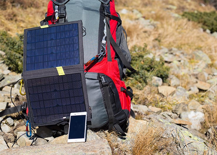 Faltbares Solarpanel lädt ein Smartphone am Rucksack während einer Outdoor-Tour in den Bergen.