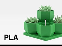  Ein 3D-gedrucktes, grünes Pflanzgefäß-Set in geometrischer Sechseckform mit Sukkulenten neben dem fettgedruckten Schriftzug „PLA“.