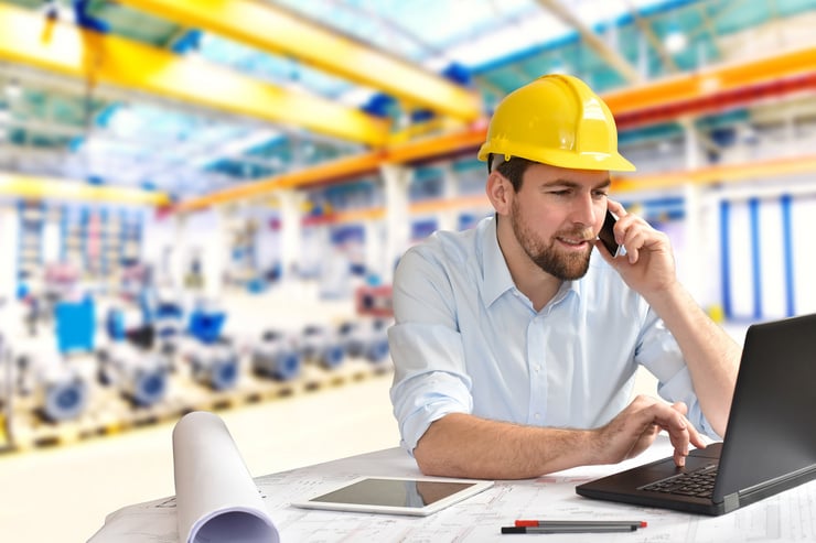 Ingenieur mit Schutzhelm bespricht am Laptop Daten zur vorausschauenden Wartung in der Produktionshalle