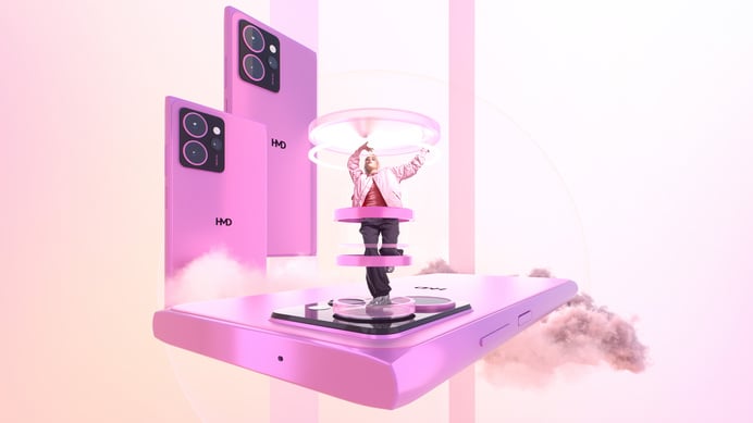 Eine schlanke, hellhäutige Person mit kurzen, hellen Haaren, bekleidet mit einer hellen Jacke, einem pinkfarbenen Oberteil und dunklen Hosen, steht mit erhobenen Armen auf einer rotierenden Plattform, die in einem überdimensionierten, hellrosa Smartphone integriert ist, während zwei weitere schwebende Smartphones ähnlicher Farbe und ein heller, wolkiger Effekt die Szene vor einem zartrosa Hintergrund ergänzen.