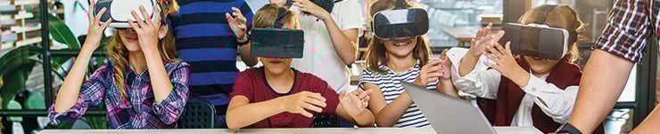 Kinder mit VR-Brillen sitzen an einem Tisch und bewegen sich spielerisch in einer virtuellen Umgebung.