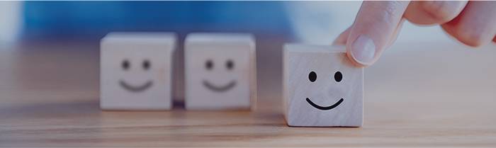 Drei Holzklötze mit Smiley-Gesichtern, Hand berührt den rechten Klotz. Zum Conrad Services.