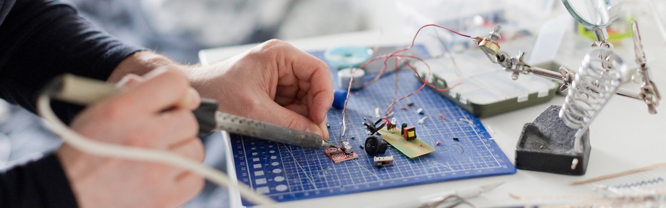 Gros plan sur une opération de brasage, au cours de laquelle une panne à souder forme une étincelle sur un circuit imprimé et est guidée avec précision par des doigts.