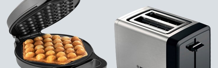 Un gril à raclette avec des aliments et un grille-pain en acier inoxydable sont placés côte à côte sur un fond gris clair.