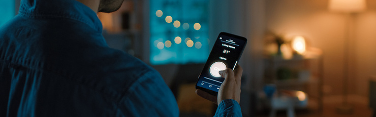 Une personne pilote l'éclairage et la température depuis un smartphone