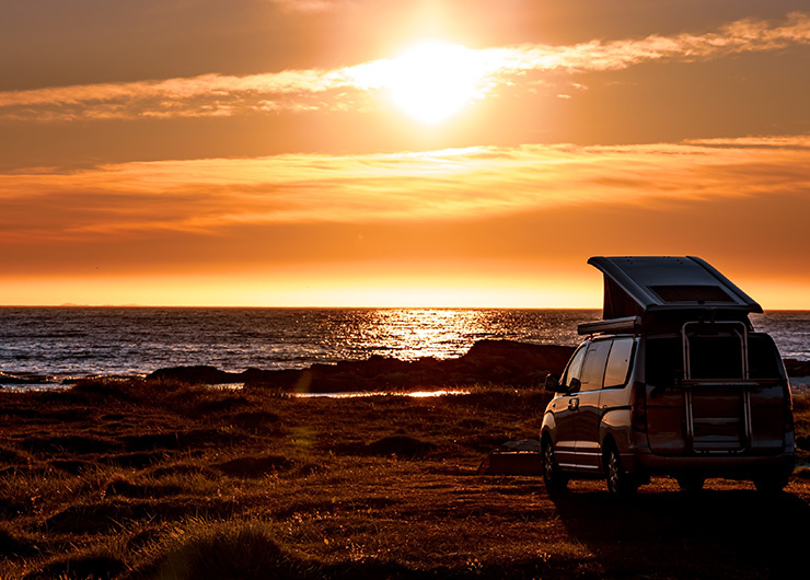 Un van aménagé est stationné au bord de la mer au coucher du soleil, le toit est relevé.
