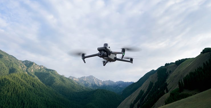 Un drone survole un paysage montagneux aux pentes verdoyantes et au ciel nuageux.