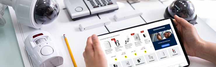 Des mains tiennent une tablette sur laquelle s'affiche une boutique en ligne spécialisée dans les équipements de sécurité et la protection contre les effractions. À l'arrière-plan, sur un bureau clair, sont disposés, en harmonie avec le thème, divers équipements de surveillance, des détecteurs de mouvement et une centrale d'alarme.