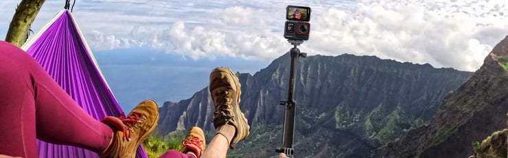Personne se relaxant dans un hamac avec vue sur un paysage montagneux, tandis qu’une caméra d’action sur trépied se tient à côté.
