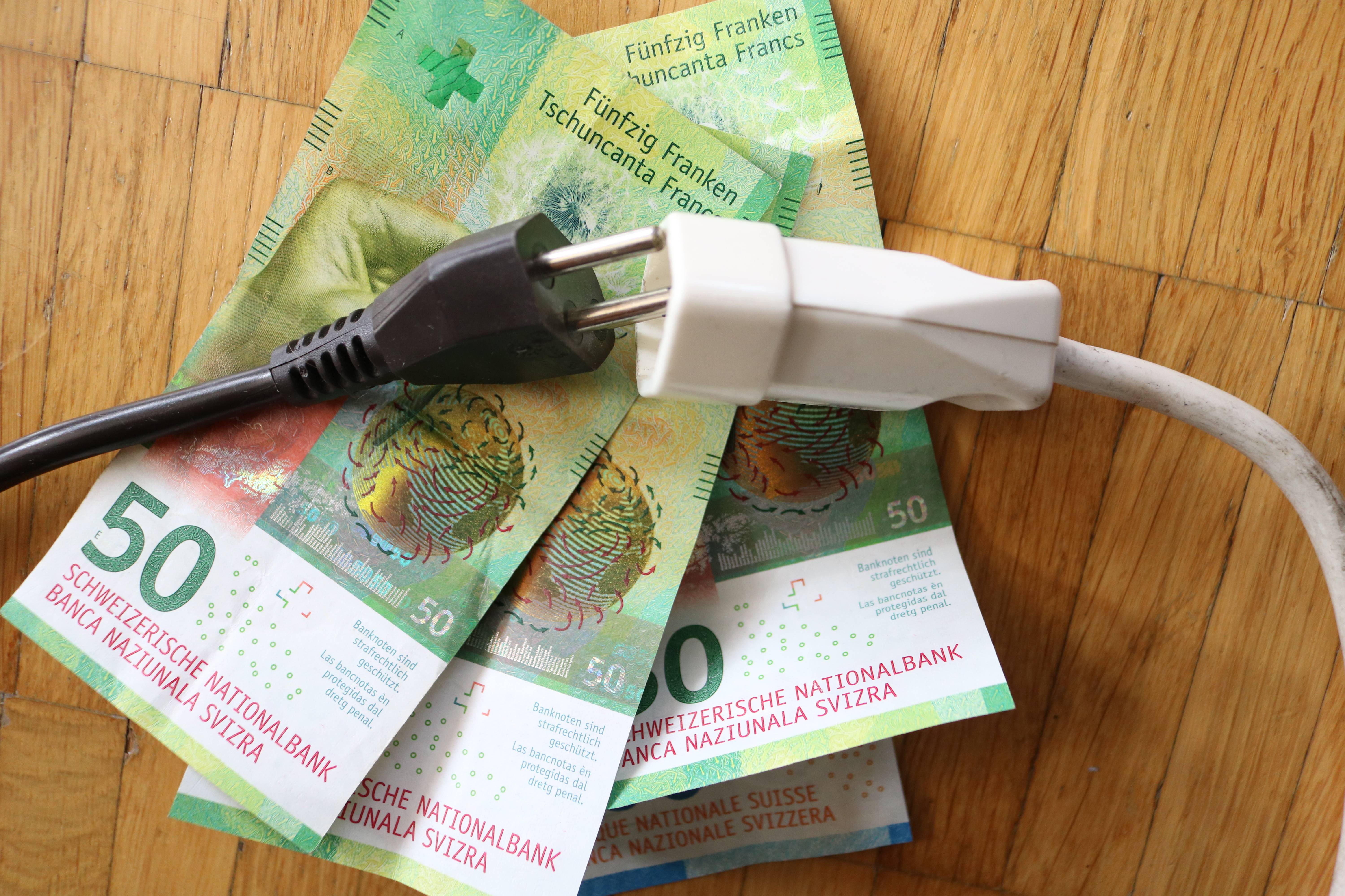 Plusieurs billets de 50 francs sont posés sur une table en bois, avec une fiche électrique noire et une fiche blanche dessus.