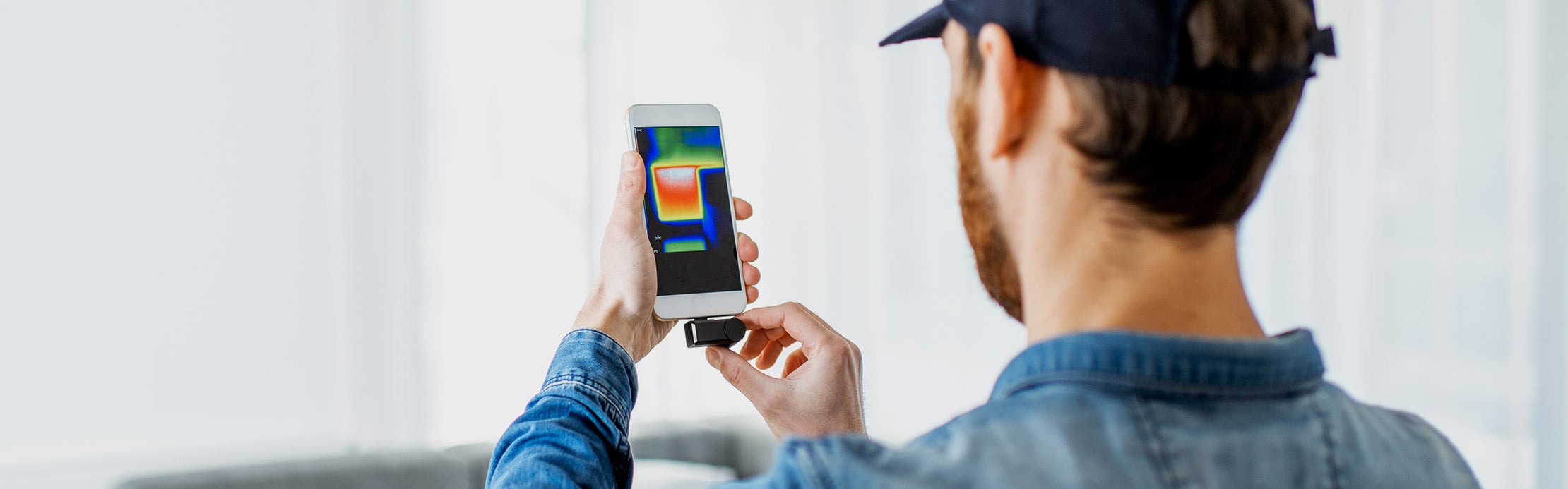 Une personne utilise une caméra thermique sur son smartphone pour mettre en évidence les différences de température et les éventuelles pertes de chaleur.