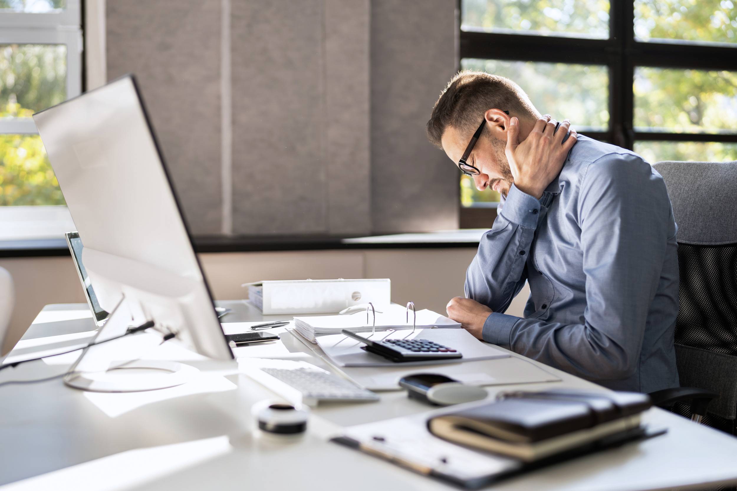 Un homme assis à un bureau, se tenant la gorge et ayant l'air stressé devant un ordinateur.