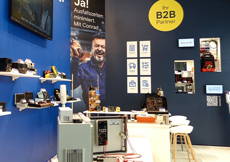 Vue latérale du stand avec le texte « Votre partenaire B2B » et « Oui ! Temps d'arrêt minimisés. Avec Conrad. »