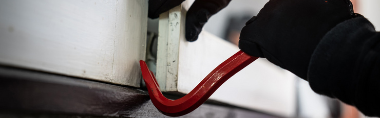 Une personne cagoulée tente de forcer une fenêtre avec un pied-de-biche rouge.