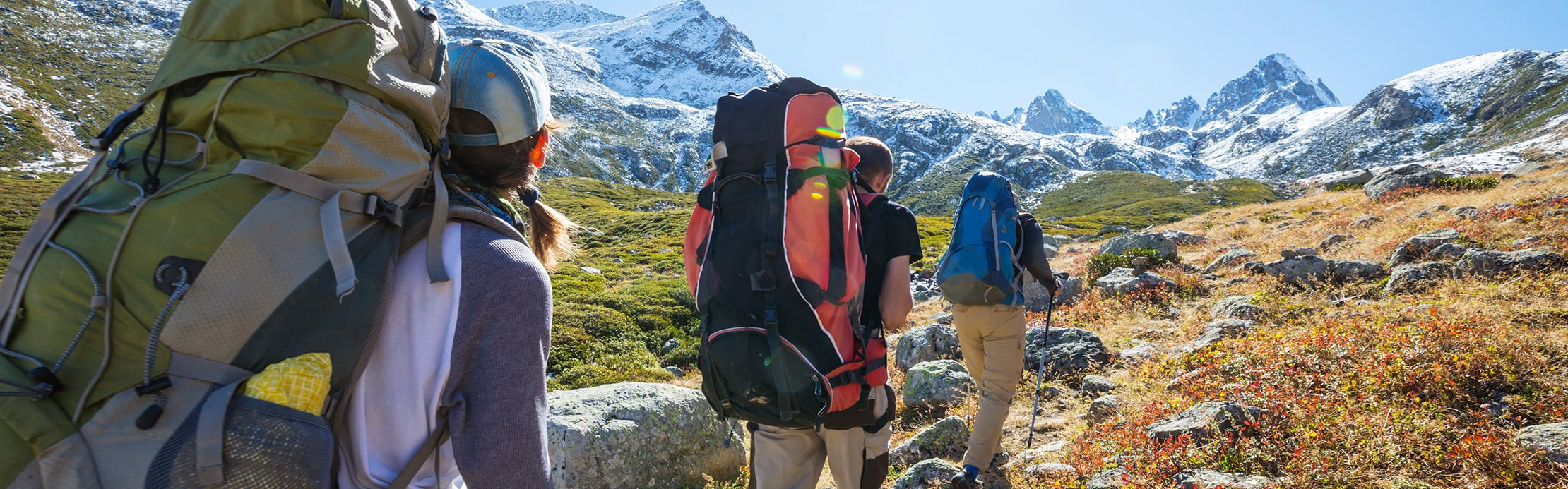 Un groupe de randonneurs, équipés de grands sacs à dos, en route dans un paysage alpin aux sommets enneigés.