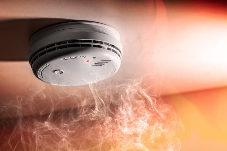 Un détecteur de fumée intelligent est fixé au plafond, sous lequel s'élève une épaisse fumée blanche.