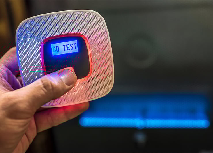 Une main tient un détecteur de monoxyde de carbone blanc et noir qui s'allume.