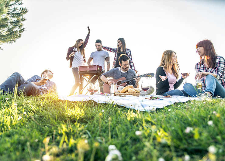 Un groupe de jeunes est assis dans un parc pour un pique-nique, tandis que certains jouent de la musique et dansent.