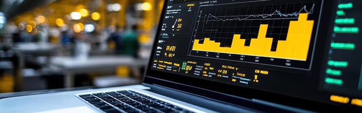 Un ordinateur portable affiche des graphiques jaunes et des données d'analyse, tandis qu'un hall de production flou est visible en arrière-plan.