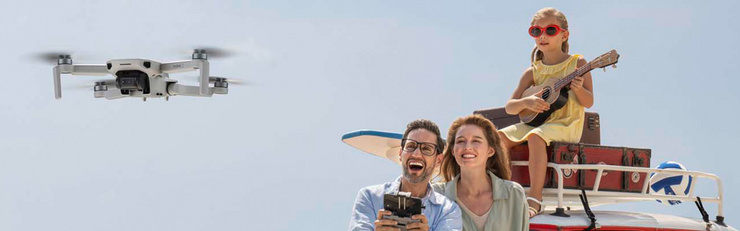 Famille avec un drone en vol, le père le pilote pendant que la fille joue du ukulélé sur le toit de la voiture.
