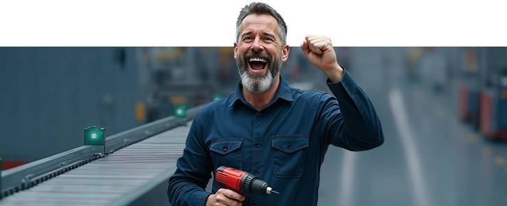 Un homme souriant avec une visseuse se tient dans un hall de production.