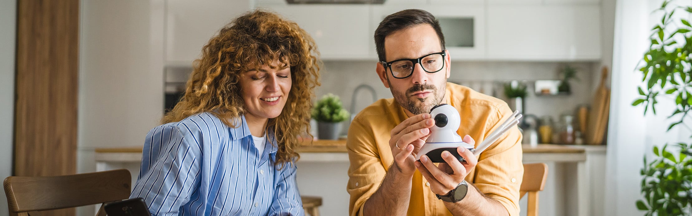 Un couple assis dans une cuisine configure ensemble une caméra de surveillance compacte.