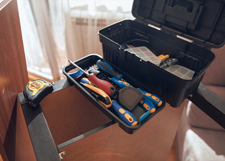 Une boîte à outils ouverte contenant divers outils est posée sur une étagère à côté d’un mètre ruban.