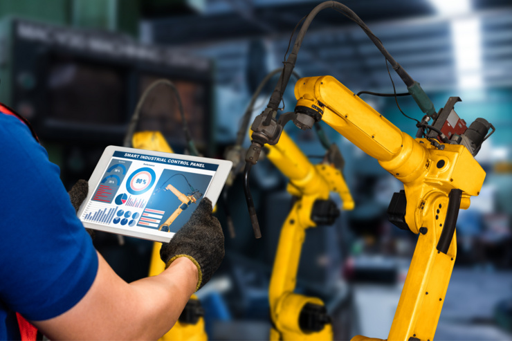 Un employé contrôle un bras robotique industriel avec une tablette dans une usine.