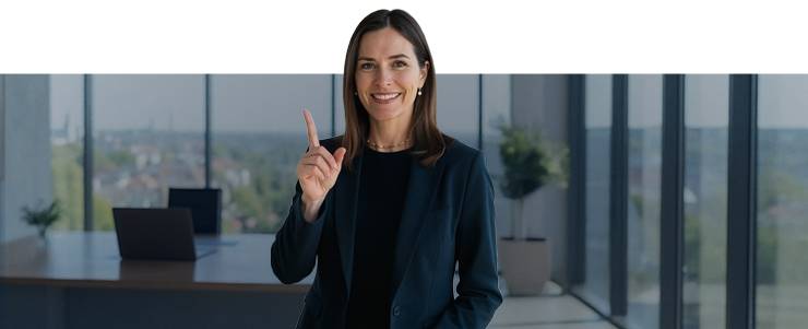 Une femme d’affaires en costume pointe le doigt vers le haut dans un bureau moderne.