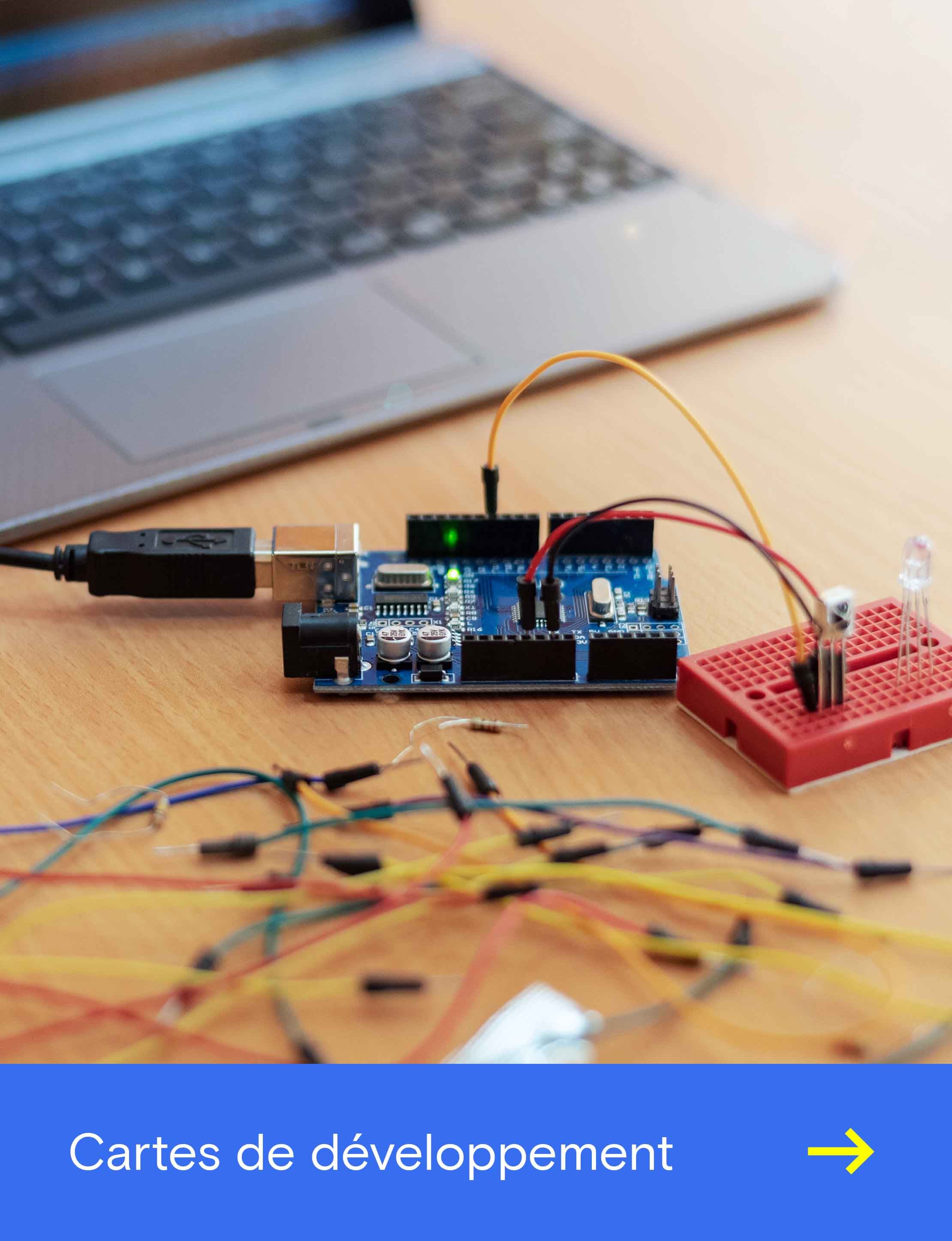 Carte de développement Arduino posée sur un bureau, connectée par USB et reliée par des câbles à une plaque d’essai rouge avec une LED.