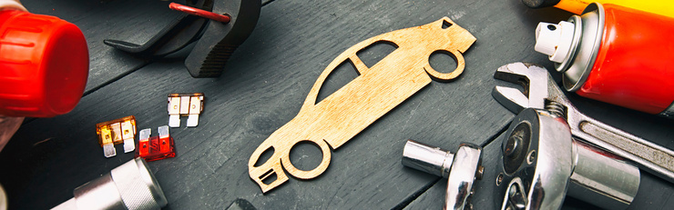 Divers outils et accessoires automobiles sont posés sur un établi à côté d’une forme de voiture en bois.