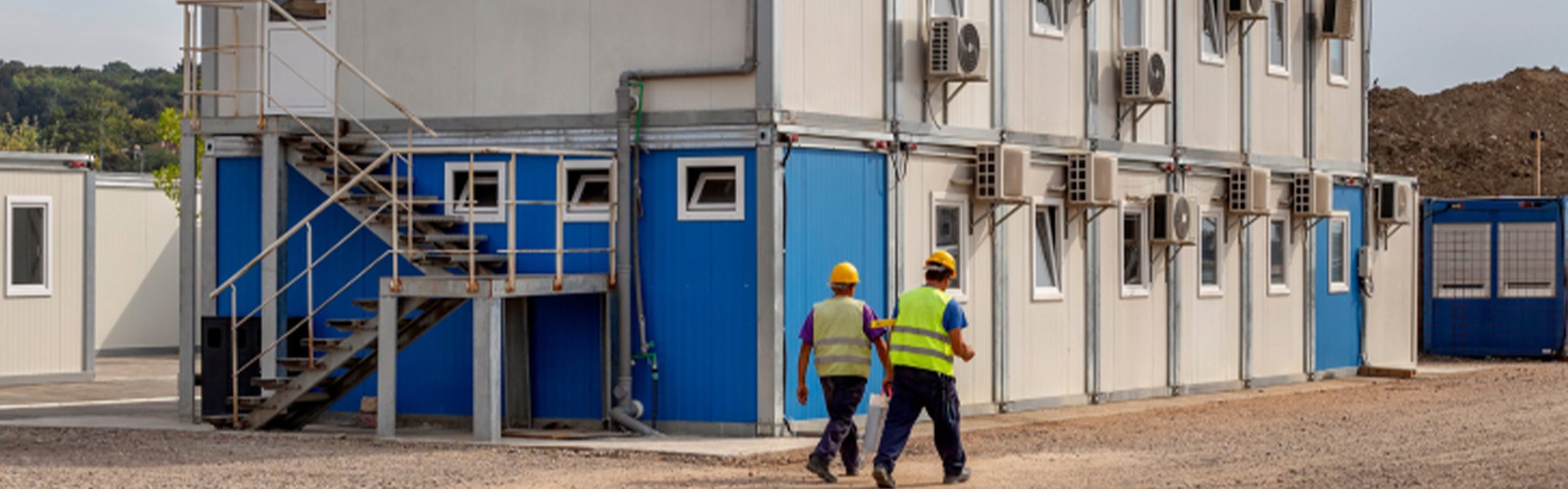 Deux ouvriers sur un chantier où on aperçoit des conteneurs de chantier