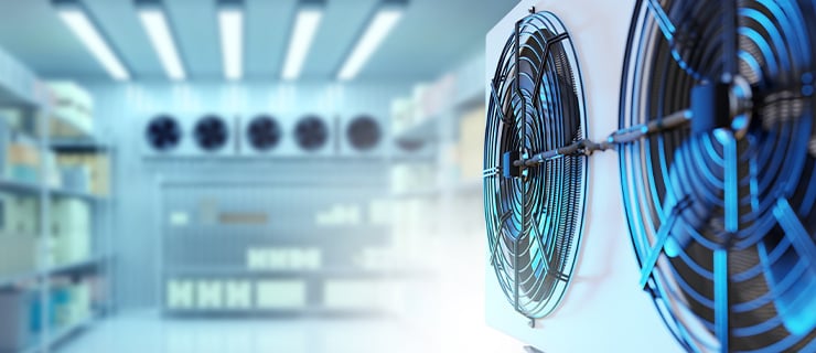 Système de climatisation industriel équipé de deux ventilateurs dans une chambre froide ; à l'arrière-plan, des rayonnages et d'autres groupes frigorifiques dans un environnement professionnel.