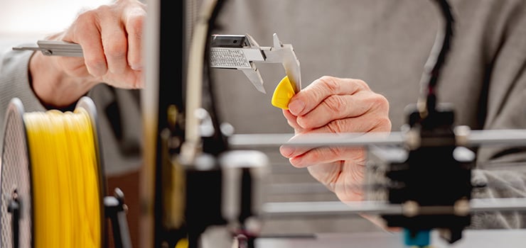 Gros plan sur une imprimante 3D et une personne mesurant une figure jaune