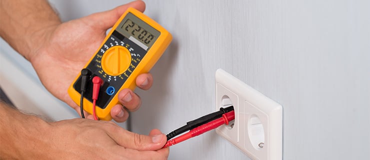 Person mesure la tension d'une prise électrique avec un multimètre numérique.