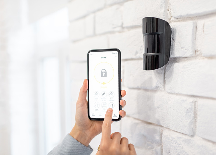 Un smartphone commande un détecteur de mouvement ou un système de sécurité installé sur le mur d'une maison.