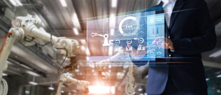 Une personne en costume utilise un panneau de contrôle numérique transparent avec des graphiques techniques dans une usine.