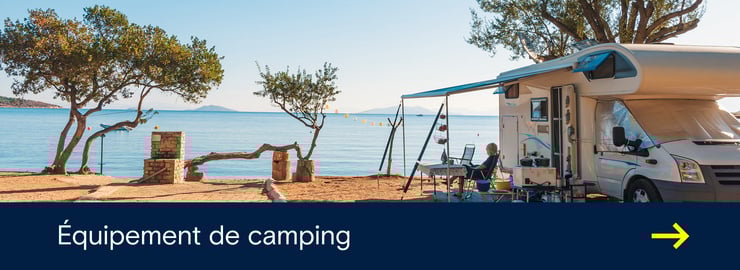 Un camping-car est garé dans un camping en bord de mer, avec un auvent, des chaises et une vue sur l'eau.