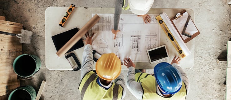 Des ingénieurs BTP portant un équipement de protection discutent des plans autour d'une table sur un chantier.