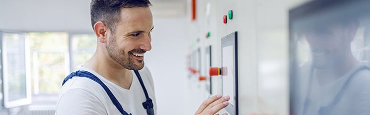 Un technicien souriant en tenue de travail utilise un panneau de commande numérique dans un local technique lumineux