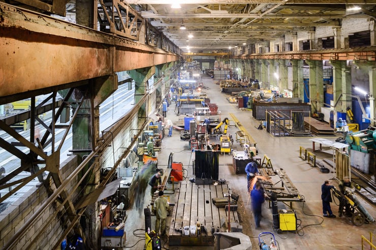 Vue d'une grande usine avec des postes de travail, des machines et plusieurs ouvriers effectuant différentes tâches.