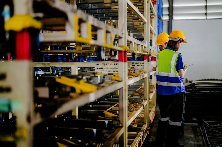 Deux travailleurs portant des casques de sécurité et des gilets réfléchissants vérifient des outils sur une étagère de stockage.
