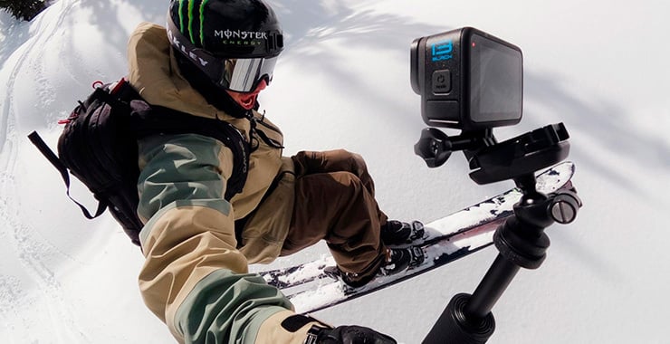 Un snowboardeur se filme pendant sa descente à l'aide d'une caméra d'action fixée sur un trépied dans la neige.